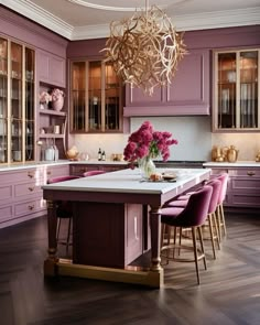 a large kitchen with purple cabinets and gold chandelier hanging from the center island