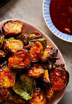 a white plate topped with brussel sprouts next to a bowl of sauce