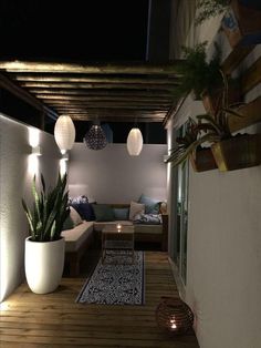 an outdoor living area with potted plants and lights on the ceiling, in front of a white wall