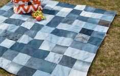 a blue and white checkered blanket sitting on top of a grass covered field next to a vase filled with fruit