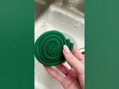 a hand holding a green cookie with a spiral design on it in front of a sink