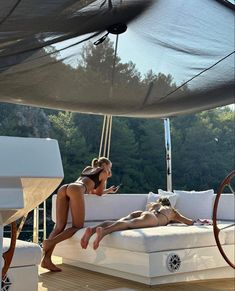 two women in bikinis are sitting on a boat with an umbrella over the deck