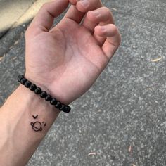 a person's arm with a small wrist tattoo on it and a black beaded bracelet around the wrist