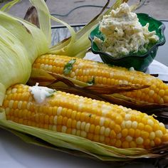 corn on the cob with butter and mayonnaise sitting on a white plate