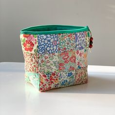 a multicolored floral print purse sitting on top of a white table next to a wall