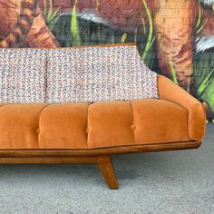 an orange couch sitting in front of a wall with a painting on it's side