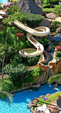 an aerial view of a water slide in the middle of a tropical garden with palm trees and thatched huts