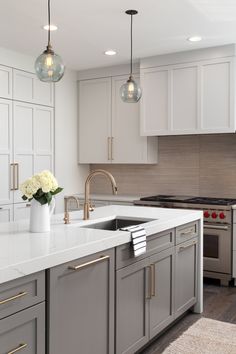 a kitchen with white cabinets and gray countertops, two hanging lights above the sink