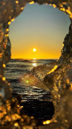 the sun is setting over the ocean as seen through an ice - covered hole in the water