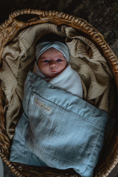 a baby wrapped in a blue blanket is sitting in a wicker basket on the floor