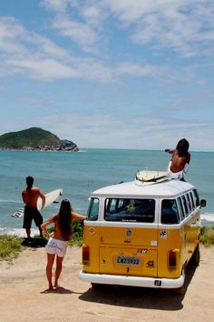 two people standing on the beach with a van and surfboard in front of them