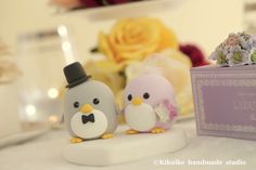 two small figurines sitting next to each other on a table with flowers in the background