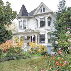 a large white house surrounded by trees and flowers