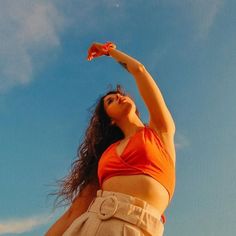 a woman in an orange top and tan skirt is flying a kite with her hands