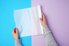 two hands are holding a piece of white paper on a blue and purple background with one hand