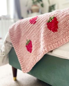 a pink knitted blanket with strawberries on it sitting on top of a bed