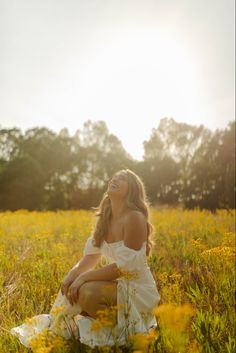 a woman is sitting in the middle of a field with yellow flowers and trees behind her