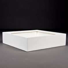 a white square box sitting on top of a gray floor next to a black wall