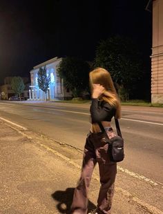 a woman walking down the street at night with her hand on her hip while talking on a cell phone