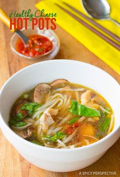 a white bowl filled with soup and vegetables on top of a wooden table next to yellow napkins