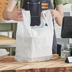 a man holding two bags while standing next to a wooden table with other items on it