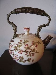 a white tea pot sitting on top of a wooden table next to a black wall