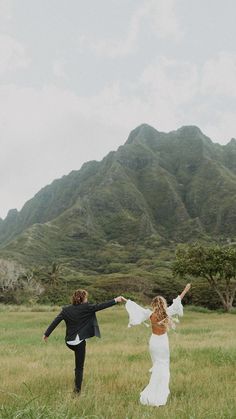 a bride and groom are running through the grass with their arms in the air as they hold each other's hands