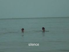 two people are swimming in the ocean with their backs turned to the camera, and one person has his head above the water's surface