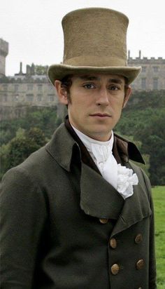 a man wearing a top hat and coat standing in front of a field with buildings