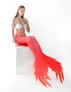 a beautiful young woman sitting on top of a white box wearing a red mermaid tail