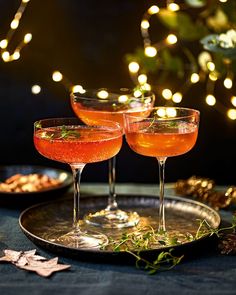 two glasses filled with drinks sitting on top of a metal tray next to christmas lights