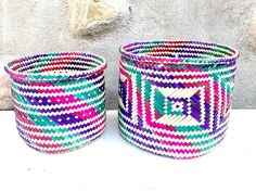 two colorful baskets sitting next to each other on a table with a stone wall in the background