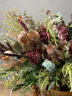 a vase filled with lots of different types of flowers and greenery on top of a wooden table