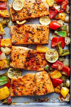 grilled salmon and vegetables on a baking sheet with lemons, tomatoes, peppers, zucchini, and onions