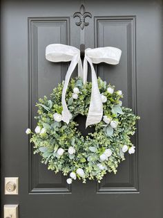 a black door with a wreath and white ribbon hanging on it's front door