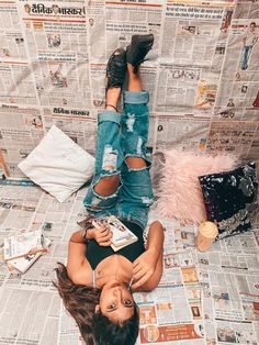 a woman laying on top of a bed next to a wall covered in newspaper paper