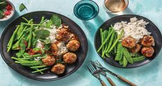 two plates with meatballs, green beans and rice next to silverware on a blue table