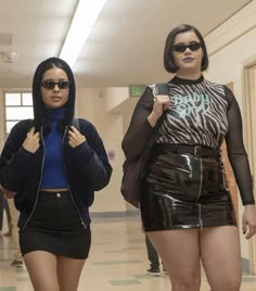 two women walking down a hallway wearing short skirts