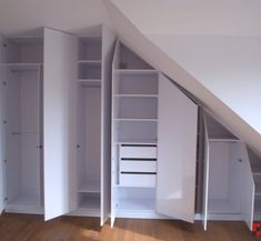 an attic bedroom with white closets and shelves in the corner, on top of a hard wood floor