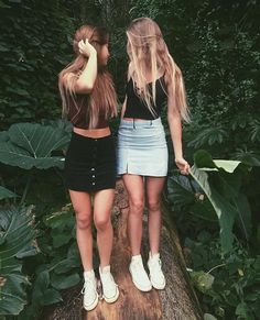 two young women standing next to each other in front of trees and plants with their hands on their heads