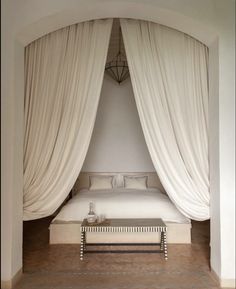 a white bed sitting under a canopy in a bedroom next to a window with drapes on it