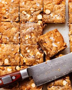 a cutting board topped with squares of brownies and nuts next to a large knife