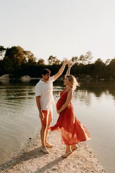 a man and woman are standing on the beach by the water with their arms in the air