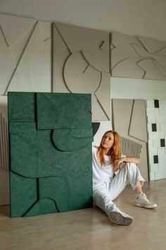 a woman sitting on the floor next to a green sculpture