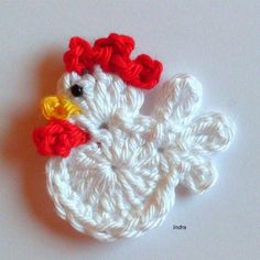 a crocheted chicken brooch sitting on top of a white table next to a red and yellow pin