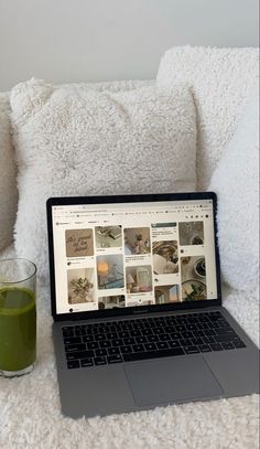 a laptop computer sitting on top of a bed next to a glass of green juice