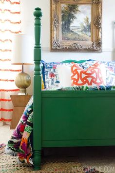 a green bed with colorful pillows and a painting on the wall in front of it