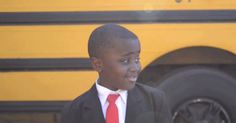 a young boy in a suit and red tie standing next to a yellow school bus