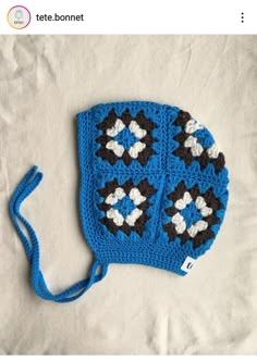 a crocheted blue and black hat with white flowers on the front, sitting on a bed