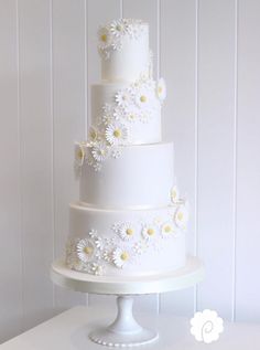 a three tiered white cake with daisies on it